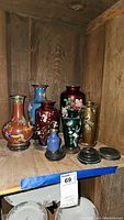 Full lot of six enameled and etched brass Asian-style vases in various colors and sizes on wood shelving.