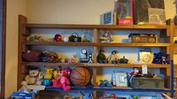 Wide shot of shelves showing Ken doll in box, plush toys including Pikachu and Pink Panther, G.I. Joe figures, and small toys including basketball and photo frame