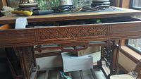 Front angled view of the carved wood table showing detailed drawer panel and carved decorative designs beneath drawer.