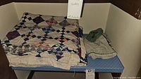 Photo showing two folded vintage patchwork quilts side by side on a blue surface with label 'Bedding'
