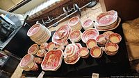Wide view of full lot on black table showing stacks of plates, cups, bowls and serving pieces