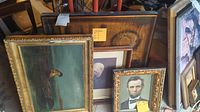 Photo showing multiple framed prints arranged closely including a vintage style portrait of Abraham Lincoln, a print of a man sitting on a dock, and other framed artworks stacked behind them.