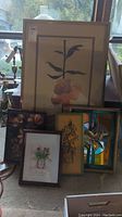 View of five framed artworks grouped together showing various floral prints and a stained glass piece