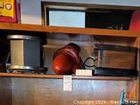 Full view of the antique fire engine siren on a shelf showing its cylindrical red metal body with some wear.