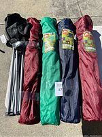 Five packed folding lawn chairs in their carrying bags arranged side by side on concrete, showing their colors and carry straps.