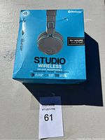 Front view of the boxed JLab Studio Wireless headphones showing model and key features.