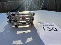 Photo showing stacked coils of the silver rope chain bracelet with various colorful gemstones including dark pink and green stones, one gem appears missing