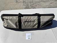 Closed Eddie Bauer beige and black fabric carrying bag for croquet set, lying flat on white table outdoors.