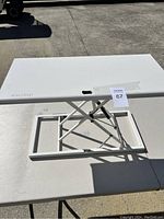 White adjustable desk riser shown in outdoor lighting, clean condition with scissor lift frame.