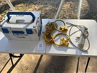 Photo of the box labeled 'Electrical Cords' alongside the yellow extension cords and the grey power strip on a white table.