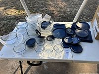 Wide shot of all glass containers and blue lids on white table outdoors, showing set variety and layout.