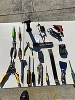 Full assortment of tools laid out on a white sheet outdoors showing various hand tools, a power drill, and electrical accessories.
