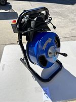 Front side view of the blue drum housing the metal cable with power cord wrapped around the frame.