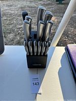 Front view of Farberware stainless steel kitchen knife set in black wooden block outdoors on white surface