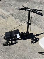 Full view of the black knee scooter showing the padded knee platform, handlebar, and wheels on concrete ground.