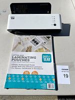 Front view of white Pen+Gear laminator with control panel and power/settings buttons, showing the laminating pouch pack in front.