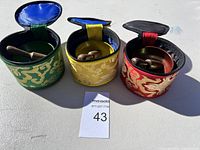 Three meditation singing bowls in green, yellow, and red fabric carrying cases, each with a wooden mallet inside.