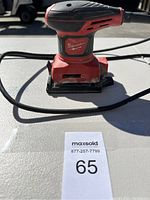 Front angled view of Milwaukee electric sander on white surface, showing the sanding pad and power cord.