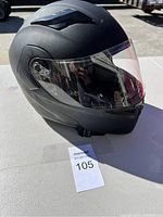Side view of matte black motorcycle helmet with clear visor showing aerodynamic vents and chin strap.