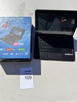 Blue retail box for Nextbook Flexx 9 showing product details and the laptop with keyboard outdoors on a white surface.