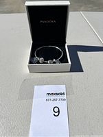 Silver Pandora bracelet with five distinct charms inside a black velvet Pandora box with lid open.