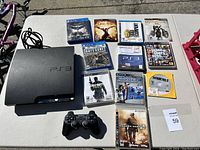 PlayStation 3 console, one controller, and ten game cases arranged on table outdoors.