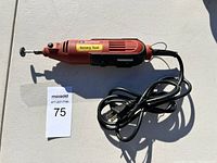 Red and black electric rotary tool lying on a flat surface. Shows full length with power cord coiled beside it, rotary bit attached, and label reading 'Rotary Tool'.