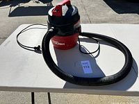 Shop Vac vacuum cleaner on white table outdoors, showing full unit and hose coiled.