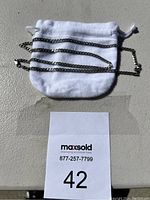 Silver necklace chain placed on a white pouch with lot number card beneath.