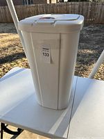 Front side view of white plastic trash can with a label and vendor tag indicating lot number 133.