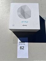 Closed box of Xfinity xFi Pod Wi-Fi extender on table surface, showing front with product illustration and logos.