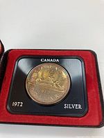 Close-up of the 1972 Canada silver dollar coin inside the black frame with red velvet lining, showing clear details and inscriptions.