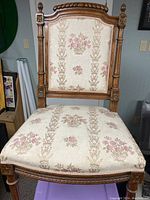 Front view showing the upholstered seat and back with floral design and carved wooden frame.