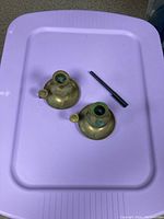Top view of two brass candleholders and one black candle snuffer on a purple surface, showing the condition and details of oxidation inside the candle cup