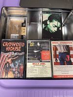 Metal tray containing multiple cassette tapes including Crowded House, Billy Joel, and Bruce Springsteen, some with original covers and others blank.