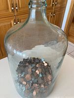 Clear view of large glass demi john bottle filled with pennies, showing height and dusty condition