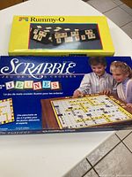 Rummy-O and Scrabble boxed games stacked on table