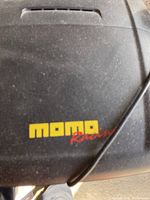 Close-up image showing the MOMO Racing logo on the racing wheel, black surface with noticeable dust.