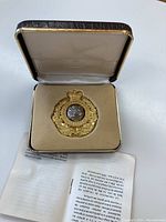 Gold plated NWMP cap badge in case with history booklet partially visible beneath