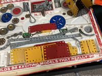 Photo of various metal strips, plates, gears, and axles laid out on a surface showing part of the Meccano set contents.