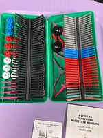 Green plastic tray containing organized colored plastic pieces for molecular modeling, including black, red, blue, white, and pink parts.