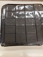 Stack of clear plastic trading card protector sheets showing front side with 20 individual pockets per sheet arranged in 4 rows by 5 columns.