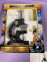 Photo of the toy microscope set packaged in box with 23 pieces, showing microscope, slides and small bottles.