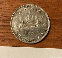 Close-up image of 1960 Canadian one dollar silver coin showing Voyageur design with canoe and paddlers, date 1960, and lettering CANADA DOLLAR.