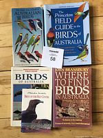Photo of four bird books for Australia arranged on a wooden surface. Includes 'The Slater Field Guide to Australian Birds', 'The Princeton Field Guide to the Birds of Australia', 'Photographic Field Guide Birds of Australia', and 'Where to Find Birds in Australia' by John Bransbury.