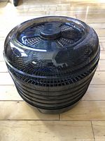 Photo of the black multi-tier food dehydrator with a transparent lid on a hardwood floor.