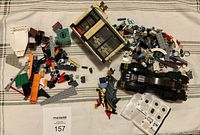 Photo of LEGO bank facade, Batmobile, Batman minifigure, and pile of miscellaneous LEGO pieces laid out on fabric surface.