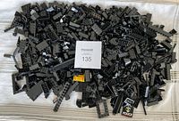 Pile of assorted black LEGO pieces including bricks, plates, windows, and specialty parts scattered over a white cloth.