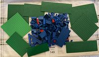 Photo showing four green LEGO baseplates and a pile of assorted blue LEGO bricks and small red pieces arranged on a fabric surface.