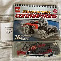Front cover of LEGO Crazy Action Contraptions activity book showing LEGO contraption featuring gears and wheels, plastic compartment below with multiple LEGO pieces in red, grey, black and white.